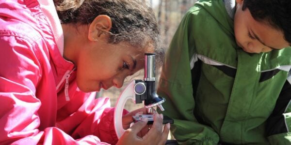 Primary school children using a microscope during a lesson outside at school