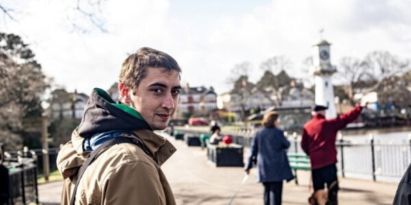 Man turns towards the camera, walking in a town, with other walkers in the background
