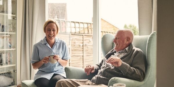 Elderly man drinking tea at home with professional carer