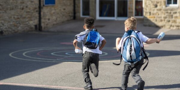 Two little boys with backpacks running into primary school