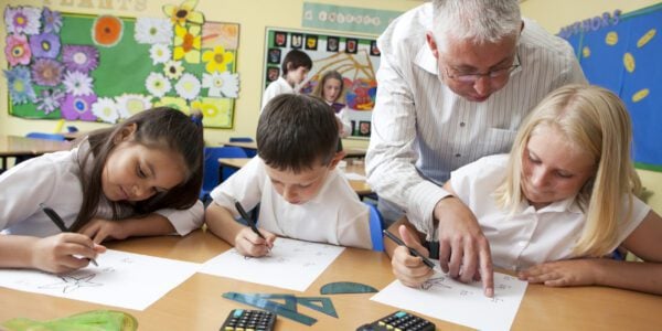 Primary school children in class writing on page with help of teacher