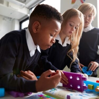 Two little boys and a little girl, all wearing primary school uniform, work together to solve a puzzle in their classroom.