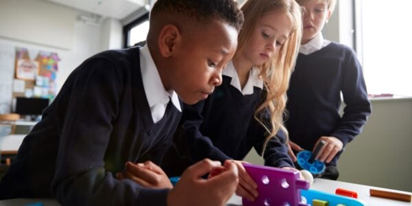 Two little boys and a little girl, all wearing primary school uniform, work together to solve a puzzle in their classroom.