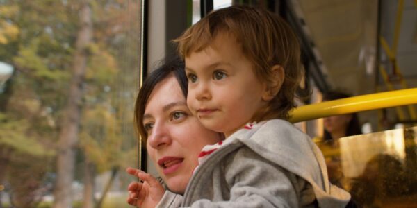 Mother and small child on a bus looking out of the window together and playing a game naming the things they see