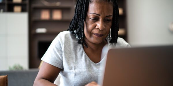 Black woman typing on laptop in living room