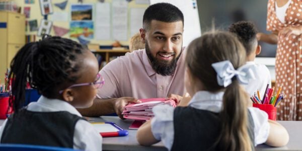 Primary school students sitting in a classroom being taught by a teacher who is crouched in front of them in the North East of England.