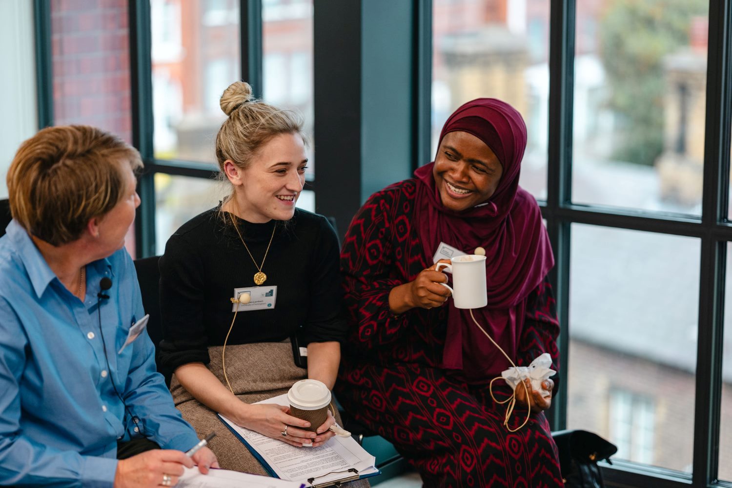 Catherine Dennison Imogen Lambert Aisha Abubakar Catherine Dennison, Imogen Lambert and Aisha Abubakar chatting and smiling over cups of coffee at the early career researcher event