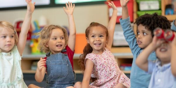 Children in preschool putting their hands up to answer a question