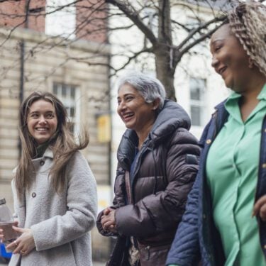 three women walking along street laughing and smiling