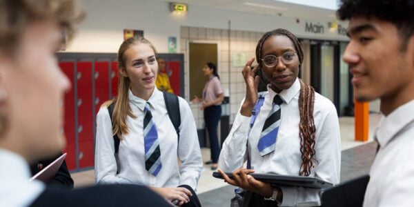 Four secondary school pupils outside school, talking to each other. Two boys and two girls, in school uniform and carrying books. One of the girls looks anxious.