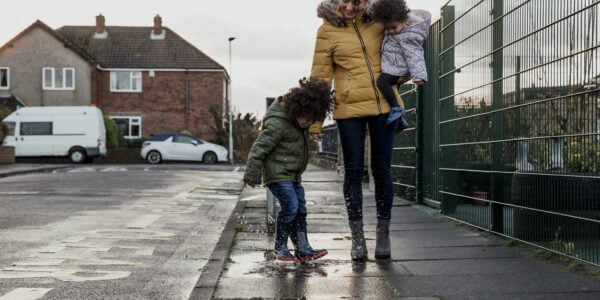 A young child splashing in a puddle next to his guardian and sister.