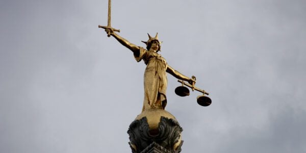 The golden statue of Lady Justice atop the famous Old Bailey law courts in London, England against a brooding stormy sky.