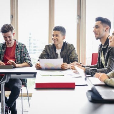 Group of students sit around a table listening.