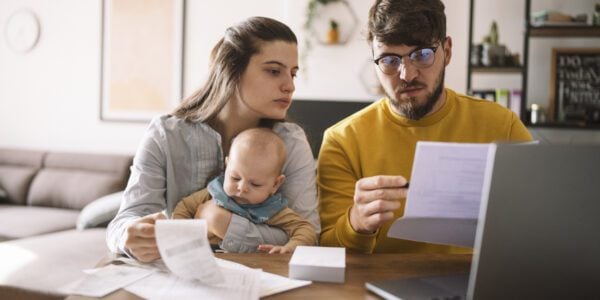 Young family with baby look at their finances at the table. They are surrounded by paperwork and a laptop.