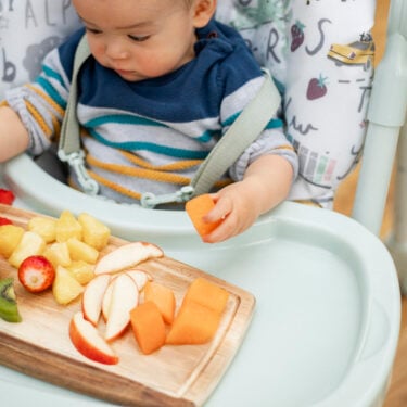 baby eating fruit on highchair