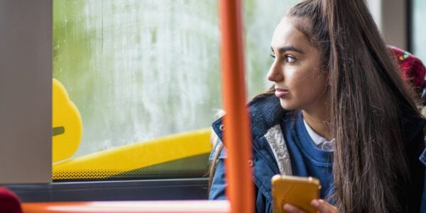 Mixed race teenage girl commuting to school holding her smartphone and looking out of the window.