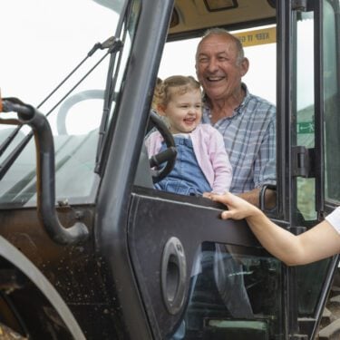 A shot of a grandfather sitting in a tractor with his young granddaughter, he is at his farm in North East, England. The grandfather and the girl's mother are teaching her about the farm.