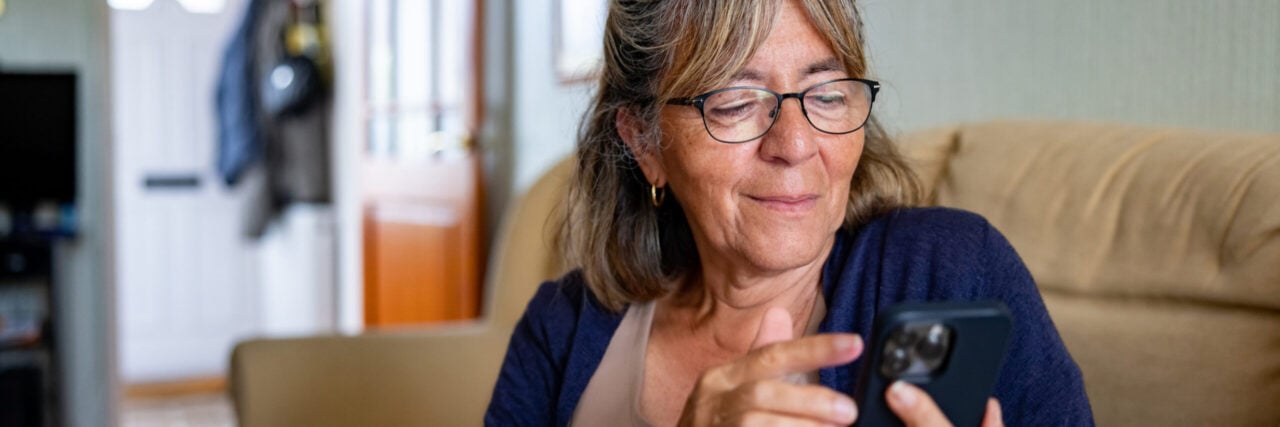 Portrait of a British woman with a visual impairment sitting on the sofa at home while using her cell phone