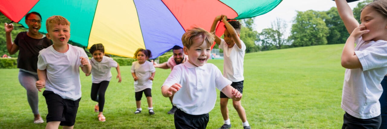 Children playing with a parachute at school during pe in the North East of England. The children are running underneath it.