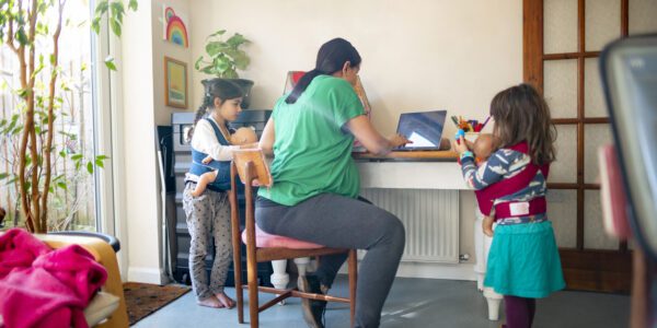 A heavily pregnant mother working at home on her laptop while talking to her kids as they stand near her.