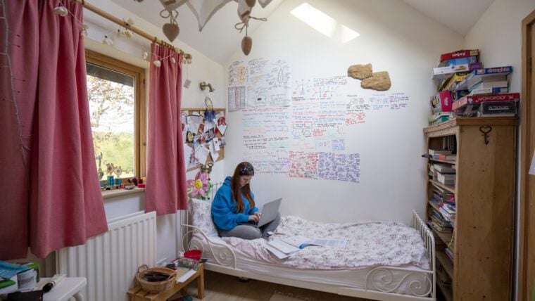 A young teenage girl does homework alone in her bedroom during the Covid 19 pandemic.