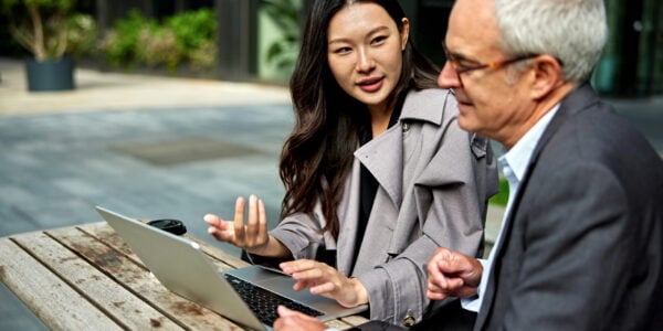 Focus on young Chinese professional sitting at table with an older man looking at laptop.