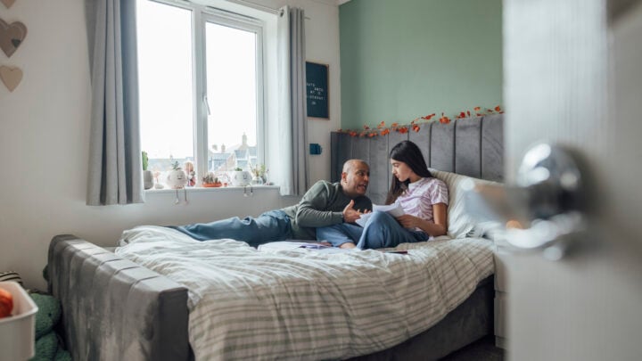Father and daughter sitting/reclining together on a bed in a bedroom at their home in the North East of England.